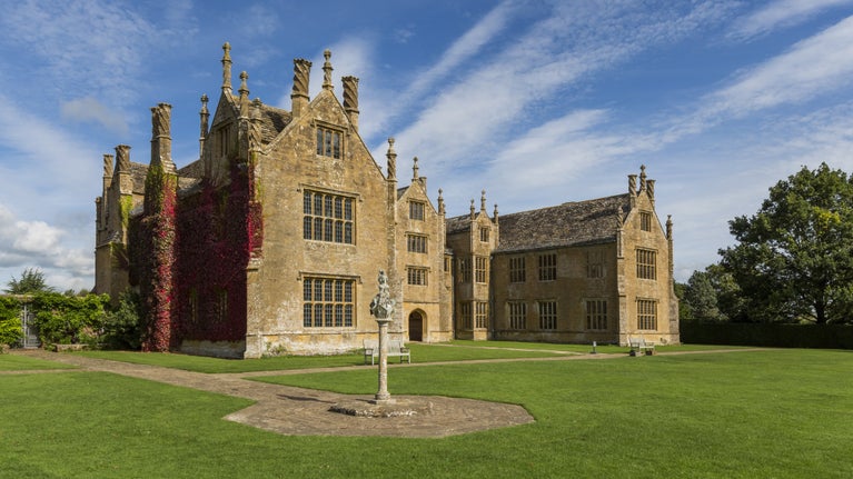 Sunny view of the 16th-century stone house of Barrington Court, with a red creeper growing up one wall